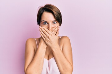 Young brunette woman with short hair over pink background shocked covering mouth with hands for mistake. secret concept.