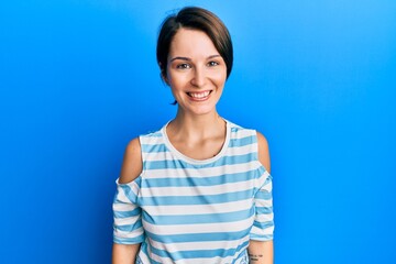 Obraz premium Young brunette woman with short hair wearing casual striped t-shirt looking positive and happy standing and smiling with a confident smile showing teeth