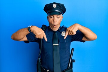 Handsome middle age mature man wearing police uniform pointing down with fingers showing advertisement, surprised face and open mouth