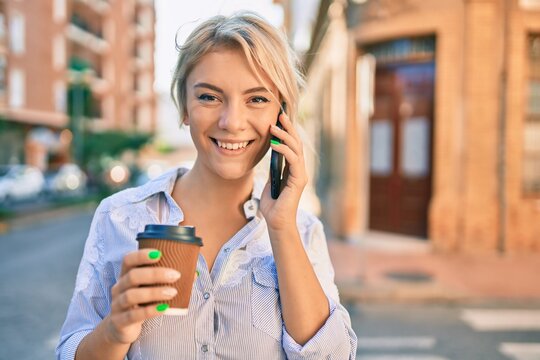 Young blonde woman smiling happy talking on the smartphone and drinking take away coffee at the city.