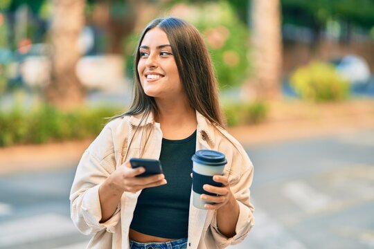 Young hispanic girl smiling happy using smartphone and drinking take away coffee at the park.