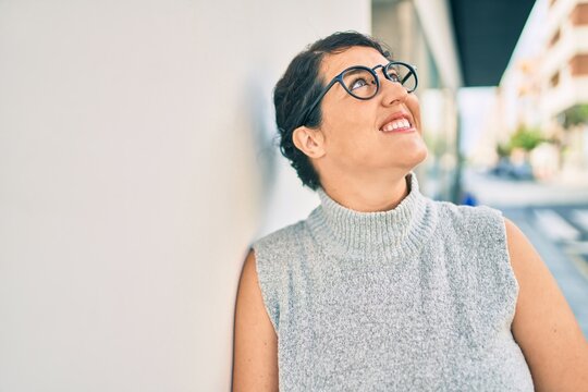 Young plus size woman smiling happy leaning on the wall at the city.