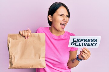 Beautiful young woman with short hair holding paper pag with express delivery text angry and mad screaming frustrated and furious, shouting with anger. rage and aggressive concept.