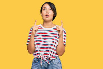 Beautiful young woman with short hair wearing casual clothes amazed and surprised looking up and pointing with fingers and raised arms.