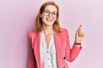 Young caucasian woman wearing business style and glasses with a big smile on face, pointing with hand finger to the side looking at the camera.