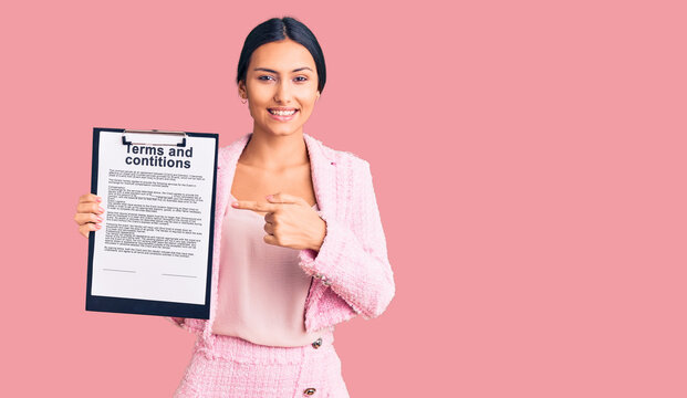 Young beautiful latin girl holding clipboard with terms and conditions document smiling happy pointing with hand and finger