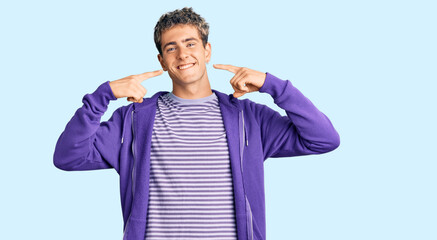 Young handsome man wearing casual purple sweatshirt smiling cheerful showing and pointing with fingers teeth and mouth. dental health concept.