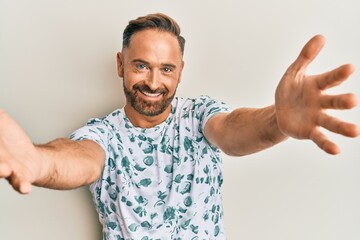 Handsome middle age man wearing casual clothes looking at the camera smiling with open arms for hug. cheerful expression embracing happiness.