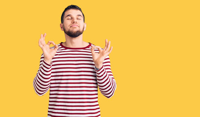 Young handsome man wearing striped sweater relaxed and smiling with eyes closed doing meditation gesture with fingers. yoga concept.