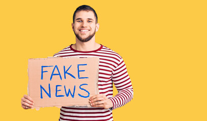 Young handsome man holding fake news message banner looking positive and happy standing and smiling...