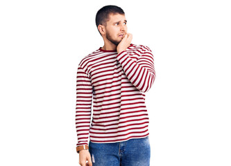 Young handsome man wearing striped sweater looking stressed and nervous with hands on mouth biting...