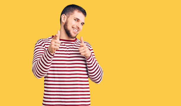 Young handsome man wearing striped sweater pointing fingers to camera with happy and funny face. good energy and vibes.