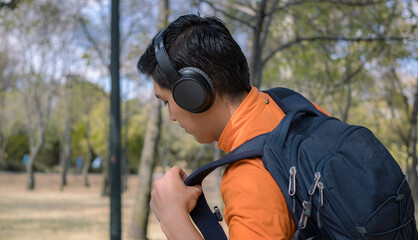 Man with headphones putting backpack on his shoulder in a park