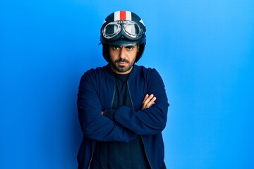 Young hispanic man holding motorcycle helmet skeptic and nervous, disapproving expression on face with crossed arms. negative person.