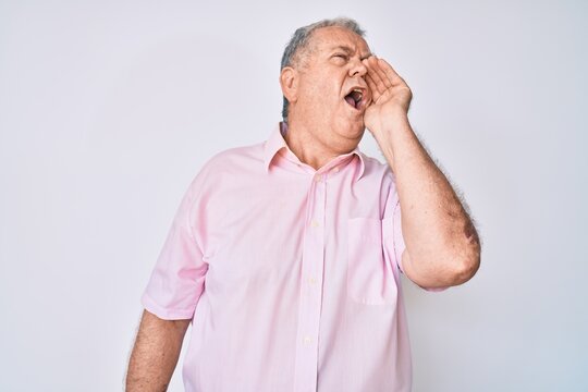 Senior grey-haired man wearing casual clothes shouting and screaming loud to side with hand on mouth. communication concept.