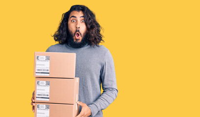 Young arab man holding delivery package scared and amazed with open mouth for surprise, disbelief face