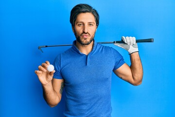 Young hispanic man holding golf ball looking at the camera blowing a kiss being lovely and sexy....