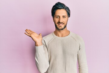 Young hispanic man wearing casual winter sweater smiling cheerful presenting and pointing with palm of hand looking at the camera.