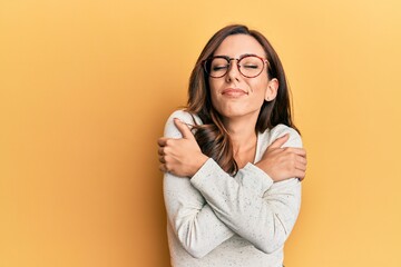 Young brunette woman wearing casual clothes and glasses hugging oneself happy and positive, smiling confident. self love and self care