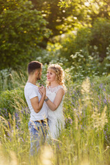Young man and woman couple walk in the meadow. Tender holding each other. Spring lovestory. Blonde-haired girl with curled hairs and man weared in casual and denim. Young family