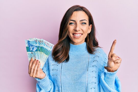 Young brunette woman holding hong kong 20 dollars banknotes smiling with an idea or question pointing finger with happy face, number one