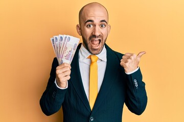 Young hispanic business man holding russian 500 ruble banknotes pointing thumb up to the side smiling happy with open mouth