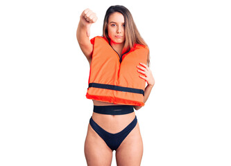 Young beautiful girl wearing life jacket with angry face, negative sign showing dislike with thumbs...