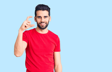 Young handsome man with beard wearing casual t-shirt smiling and confident gesturing with hand doing small size sign with fingers looking and the camera. measure concept.