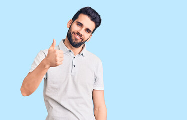 Young handsome man with beard wearing casual polo doing happy thumbs up gesture with hand. approving expression looking at the camera showing success.