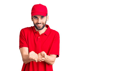 Young handsome man with beard wearing delivery uniform smiling with hands palms together receiving or giving gesture. hold and protection