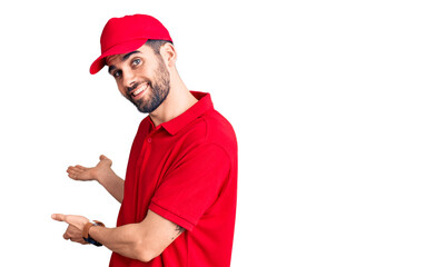 Young handsome man with beard wearing delivery uniform inviting to enter smiling natural with open...