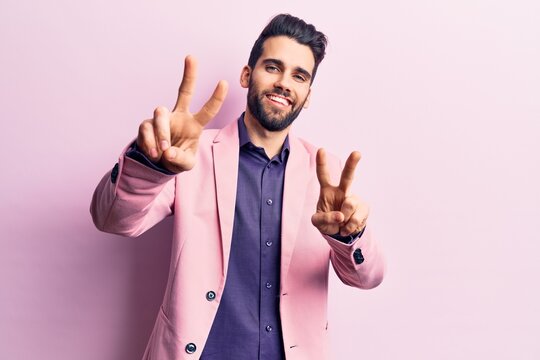 Young handsome man with beard wearing elegant jacket smiling looking to the camera showing fingers doing victory sign. number two.