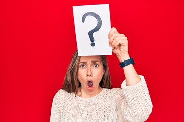 Young beautiful blonde woman holding question mark over head scared and amazed with open mouth for surprise, disbelief face