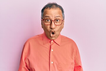 Middle age indian man wearing casual clothes and glasses afraid and shocked with surprise expression, fear and excited face.