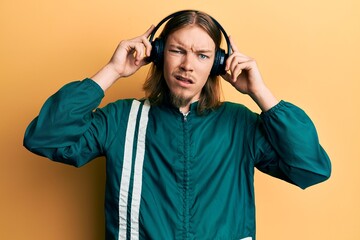 Handsome caucasian man with long hair wearing gym clothes and using headphones in shock face,...