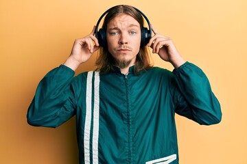 Handsome caucasian man with long hair wearing gym clothes and using headphones skeptic and nervous,...