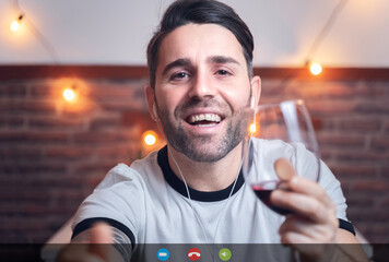 Photo of a screen, during a video call, of a young man, toasting with a glass of red wine, through...