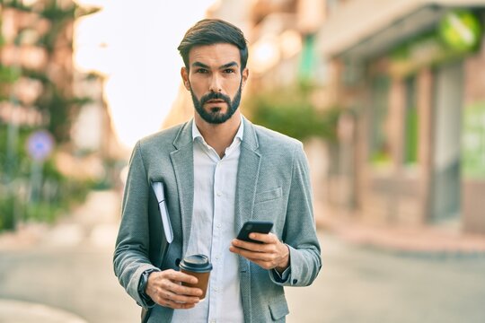 Young hispanic businessman with serious expression using smartphone and drinking coffee at the city.