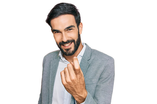 Young hispanic man wearing business clothes beckoning come here gesture with hand inviting welcoming happy and smiling