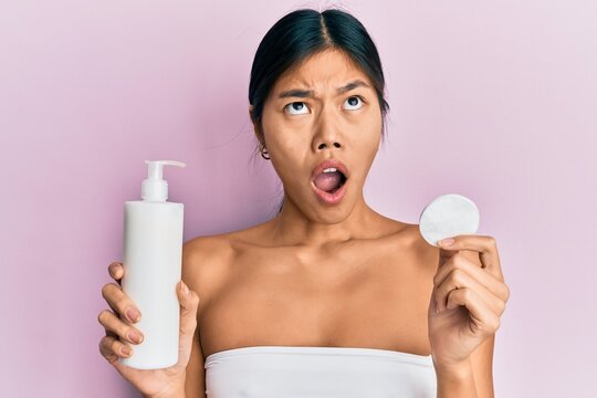 Young chinese woman wearing shower towel using clean lotion angry and mad screaming frustrated and furious, shouting with anger looking up.
