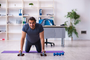 Fototapeta premium Young handsome employee doing sport exercises in the office