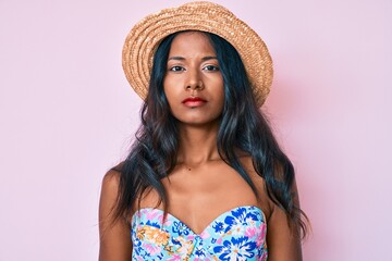 Young indian girl wearing bikini and summer hat with serious expression on face. simple and natural looking at the camera.