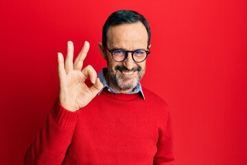 Naklejka premium Middle age hispanic man wearing casual clothes and glasses smiling positive doing ok sign with hand and fingers. successful expression.