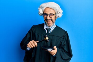 Middle age hispanic man using gavel winking looking at the camera with sexy expression, cheerful...
