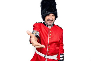 Middle age handsome wales guard man wearing traditional uniform over white background smiling cheerful offering palm hand giving assistance and acceptance.