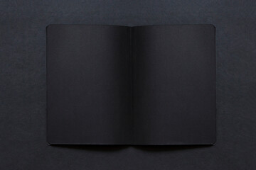 Cuaderno abierto  color negro sobre fondo negro. Espacio libre para texto o fotos.