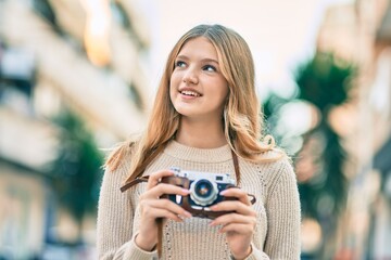 Beautiful caucasian teenager smiling happy using vintage camera at the city.