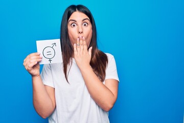 Young beautiful woman asking for sex discrimination holding paper with gender equality concept covering mouth with hand, shocked and afraid for mistake. Surprised expression