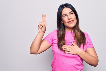 Young beautiful brunette woman wearing casual pink t-shirt standing over white background smiling swearing with hand on chest and fingers up, making a loyalty promise oath