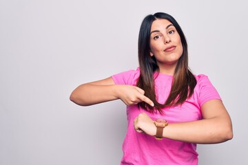 Young beautiful brunette woman wearing casual pink t-shirt standing over white background In hurry...